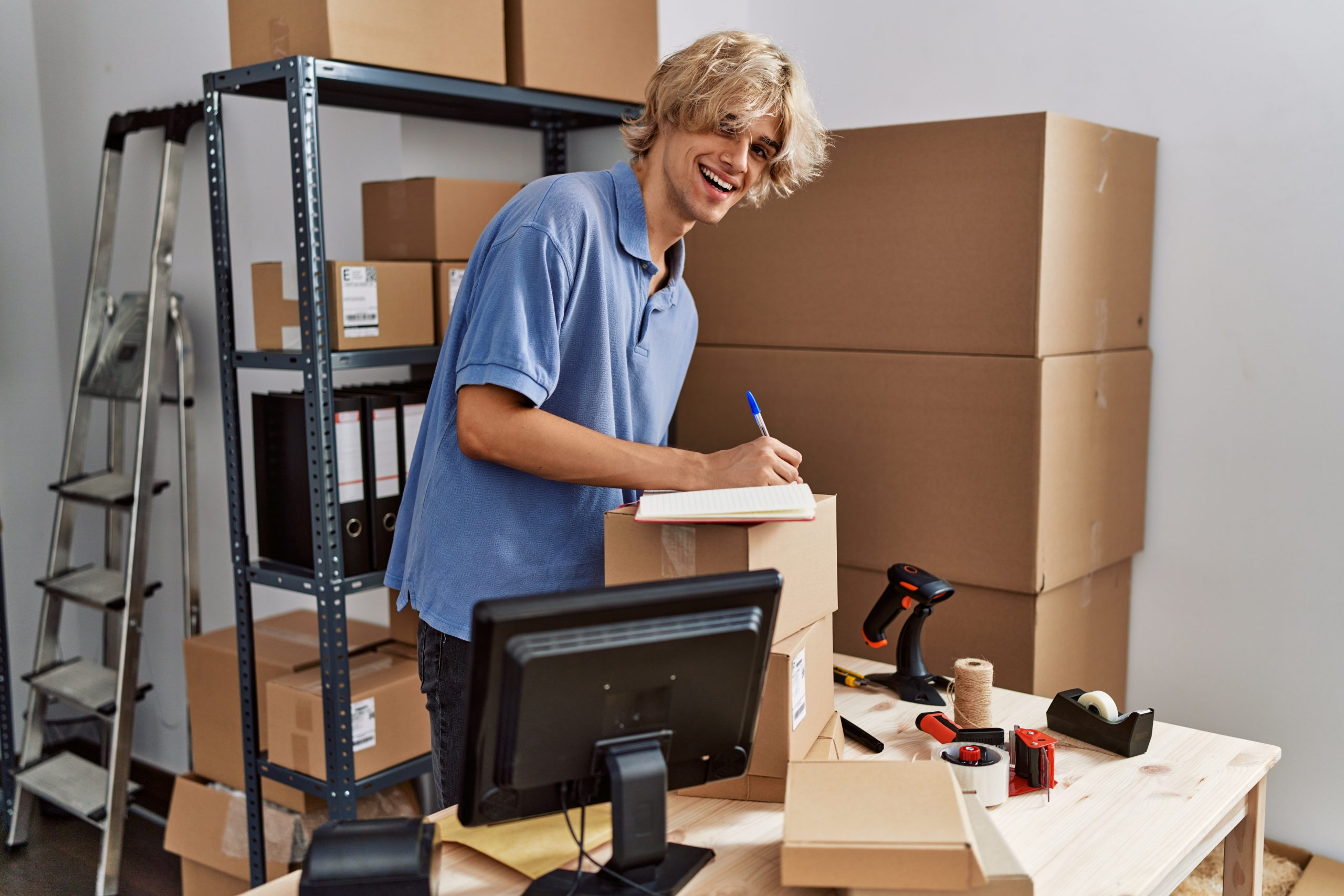 Smiling worker taking inventory notes among packed moving boxes